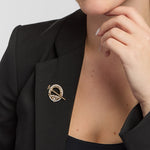 A gold Tara brooch, intricately encrusted with diamonds, is elegantly pinned to a black blazer worn by a female model
