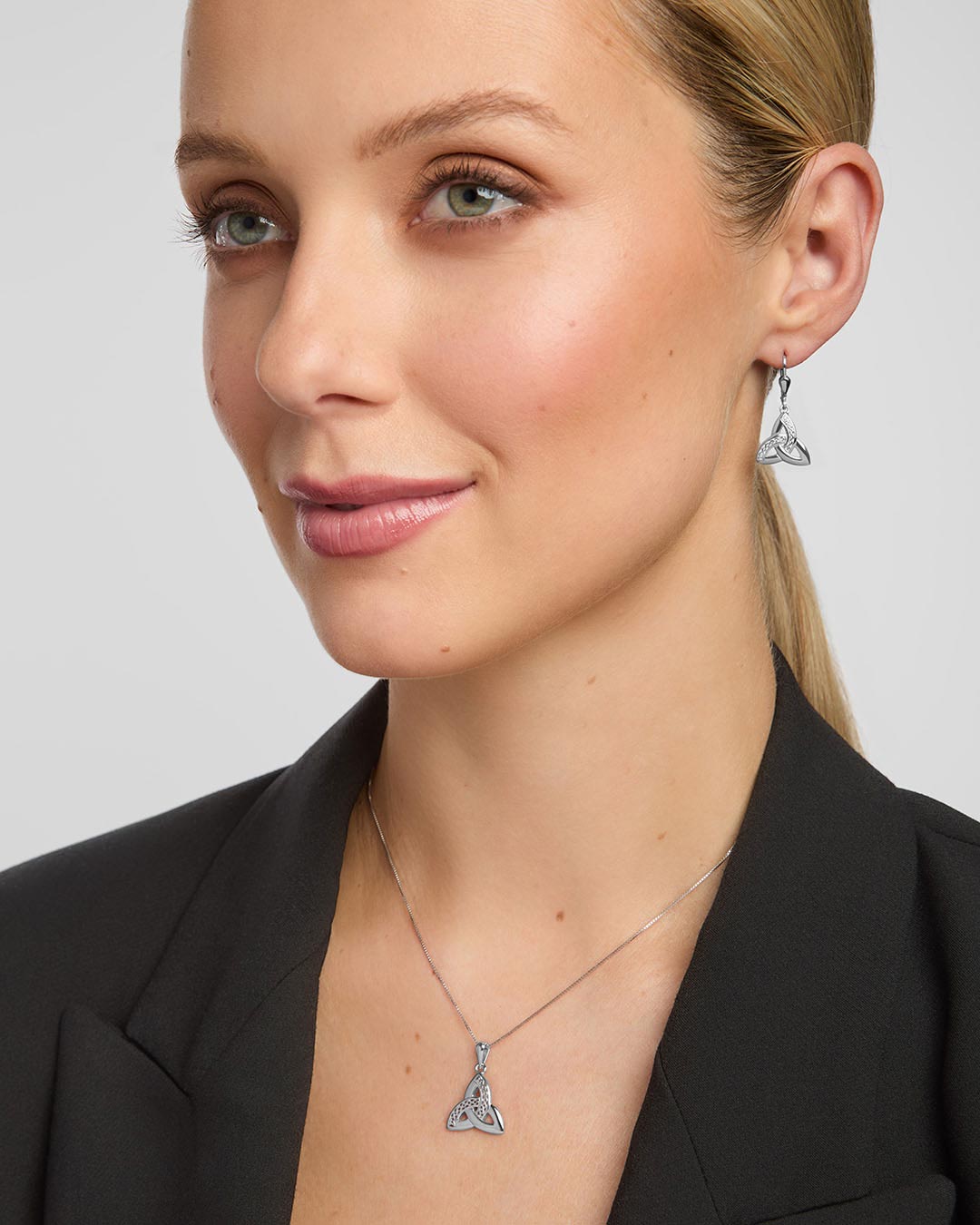 a female model wearing matching celtic trinity knot pendant and earrings set in sterling silver