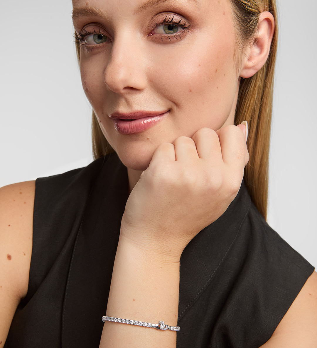 Woman wearing a silver Claddagh cz tennis bracelet on a plain background