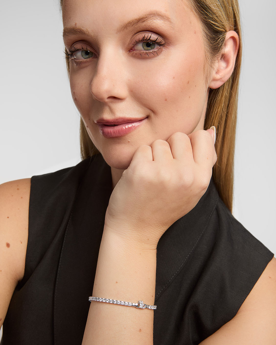 Woman wearing a silver Claddagh cz tennis bracelet on a plain background
