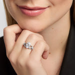 A close-up lifestyle shot of a woman wearing a silver Claddahg ring with a central white stone heart, resting her chin on her hand.