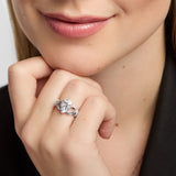 A close-up lifestyle shot of a woman wearing a silver Claddahg ring with a central white stone heart, resting her chin on her hand.