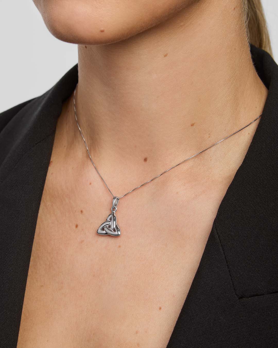 Silver necklace with a double-sided trinity knot pendant on a person wearing a black blazer.