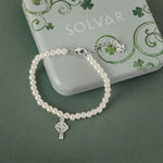 Celtic pearl bracelet with a silver Celtic cross charm on a green background