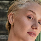 Close-up of a woman wearing gold Claddagh earrings with a blurred background