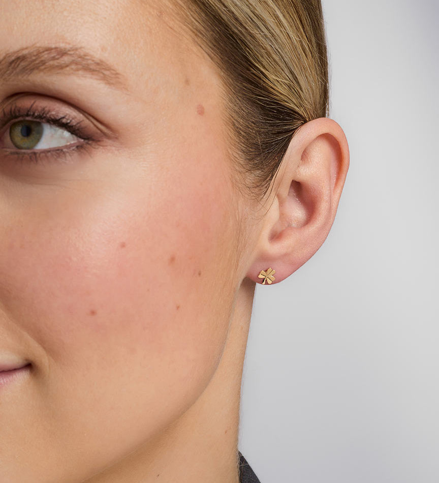 close-up image of gold shamrock stud earrings on a model