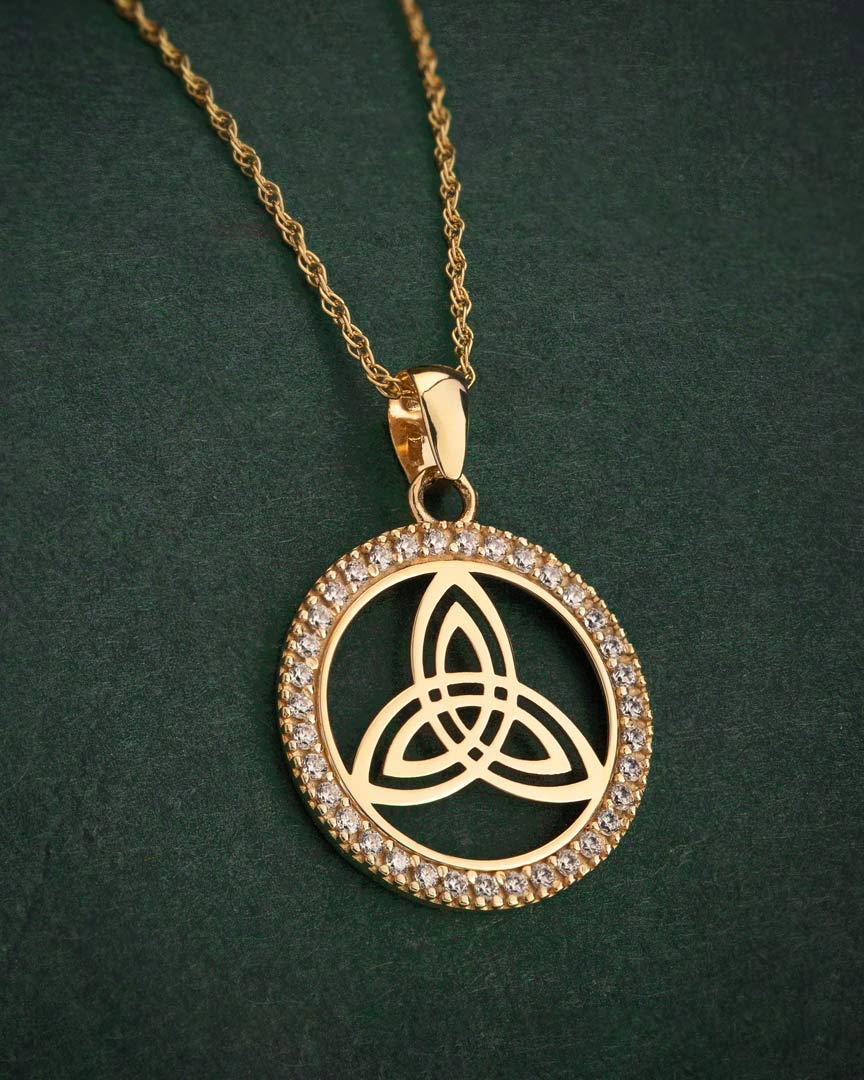 lifestyle image of yellow gold trinity knot round necklace on green background