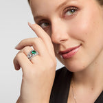 Green Cz Celtic Claddagh Band Ring, featuring a vivid green gemstone and sparkling accents, worn on a hand positioned beside the face against a light grey background.