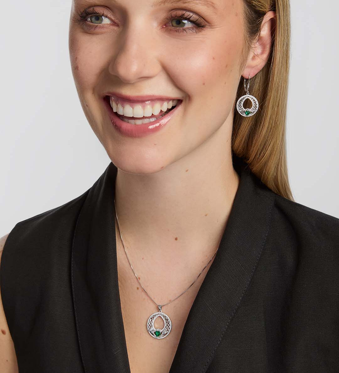 a female model wearing matching celtic Claddagh necklace and earrings with a green cubic zirconia Claddagh heart