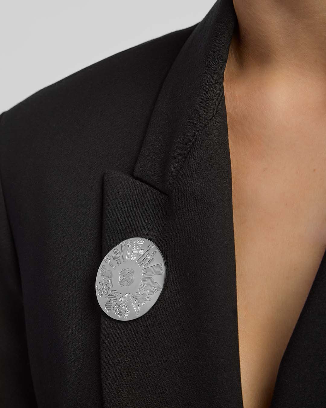 Black blazer with a silver History of Ireland round brooch on a neutral background