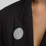 Black blazer with a silver History of Ireland round brooch on a neutral background