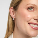 A close-up of a woman's wearing a small gold Trinity Knot stud earrings with a clear teardrop-shaped Lab diamond, set against a light grey background.