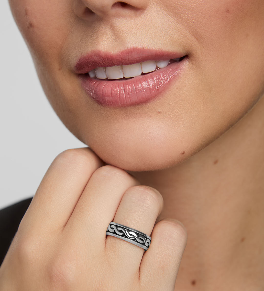Close-up of a woman wearing a silver Celtic band ring on a neutral background