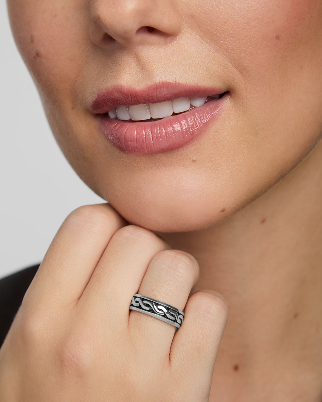 Close-up of a woman wearing a silver Celtic band ring on a neutral background