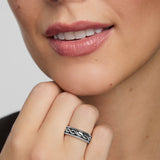 Close-up of a woman wearing a silver Celtic band ring on a neutral background
