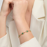A close-up of a model wearing gold Celtic bracelet with oval real emerald gemstones and decorative knotwork links,