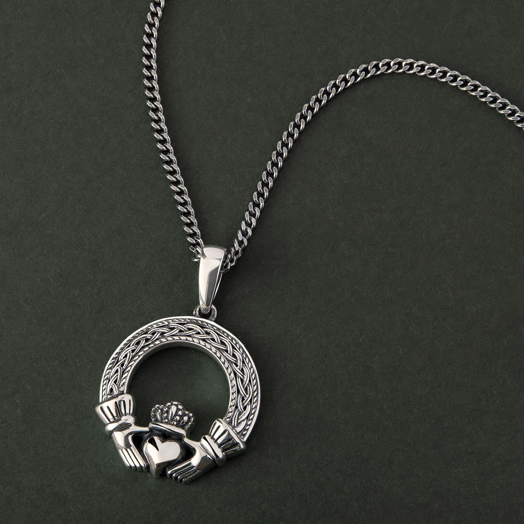 lifestyle image of mens celtic claddagh pendant with a heavy chain on a dark background 
