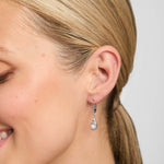 Close-up of a woman wearing a pearl Trinity Knot drop earring with a plain background