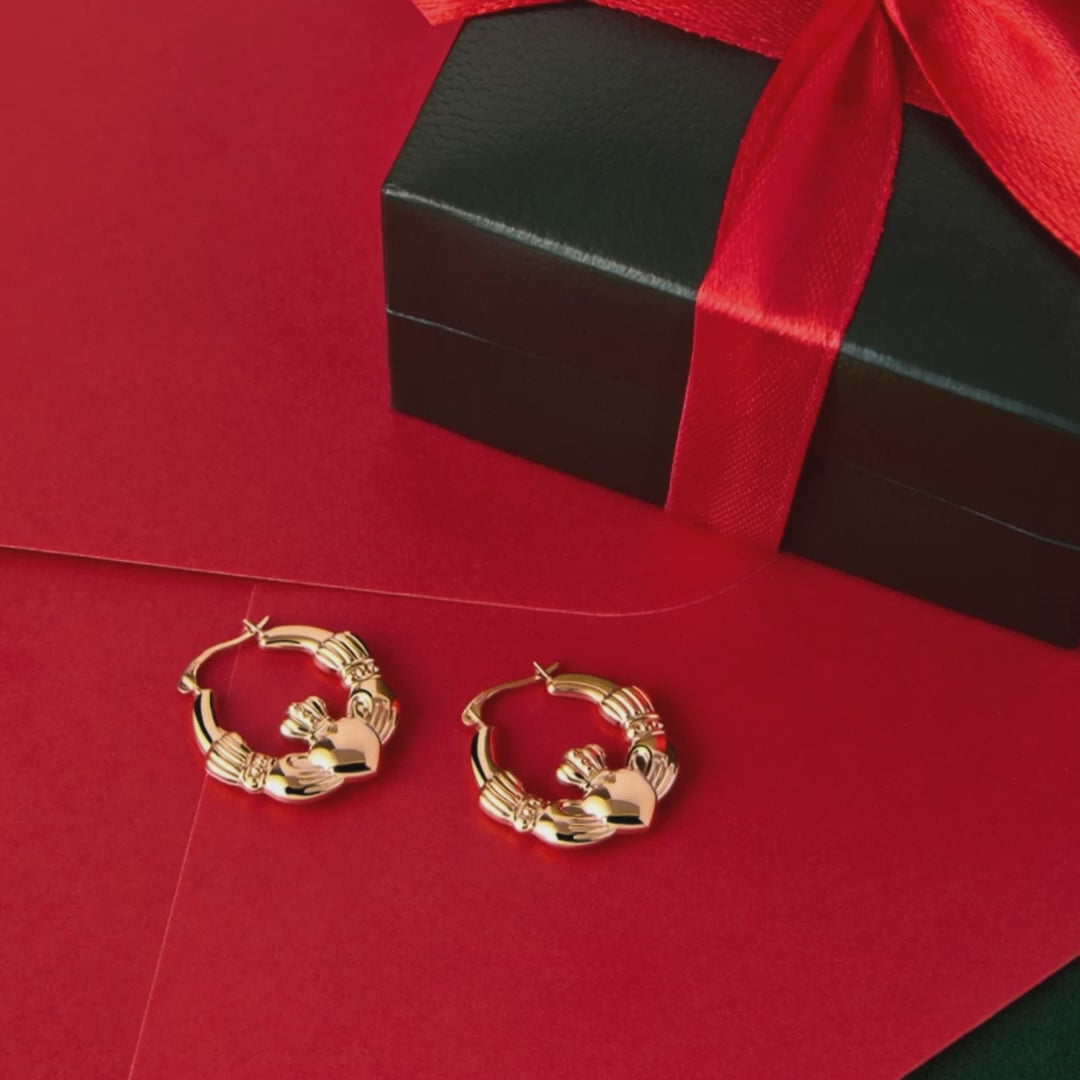 A close-up of gold Claddagh hoop earrings resting beside a jewellery box, captured on a rotating display to show their detail and shine