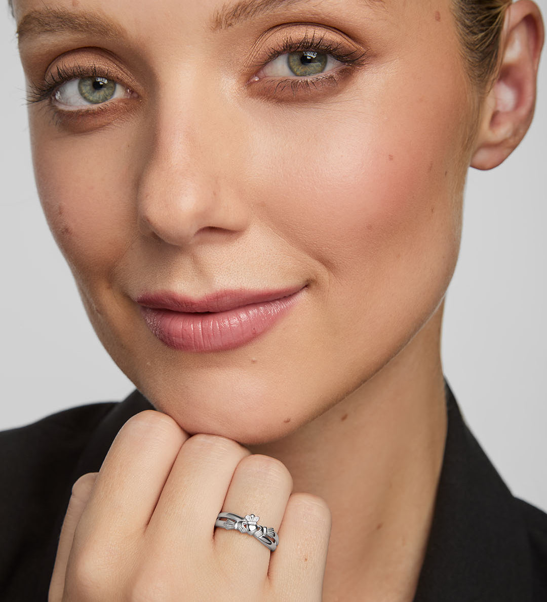 Close-up of a woman wearing a silver Claddagh ring on a plain background