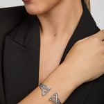 Silver bracelet with a Celtic knot design on a woman's wrist against a black background
