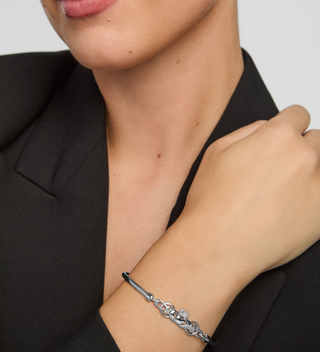 Close-up of a woman wearing a silver Claddagh bangle bracelet on a plain background