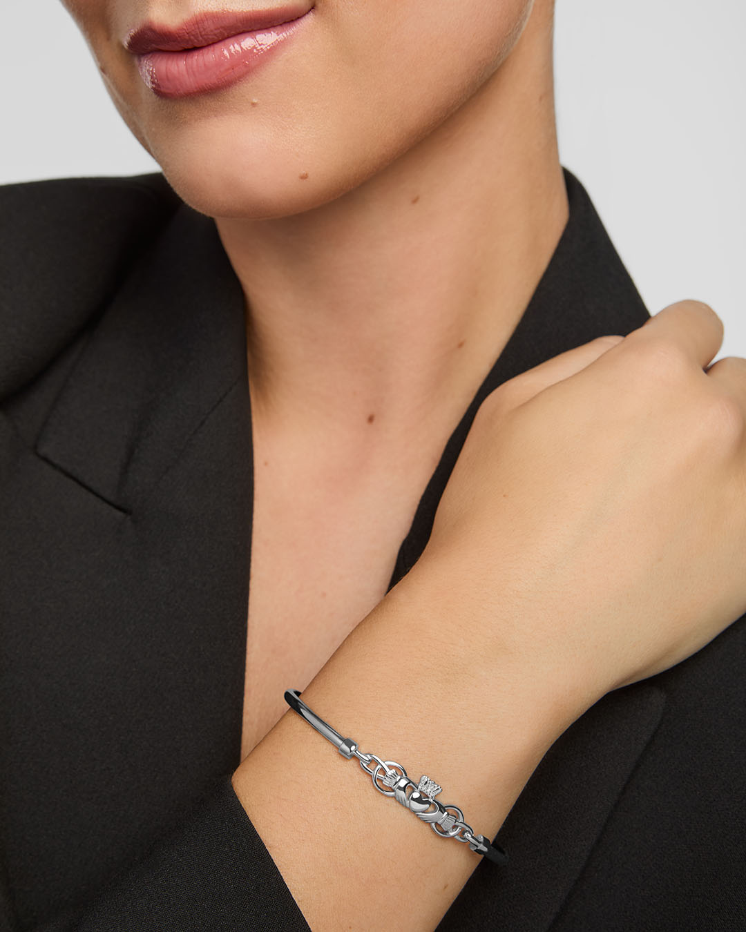 Close-up of a woman wearing a silver Claddagh bangle bracelet on a plain background