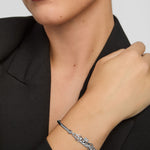 Close-up of a woman wearing a silver Claddagh bangle bracelet on a plain background