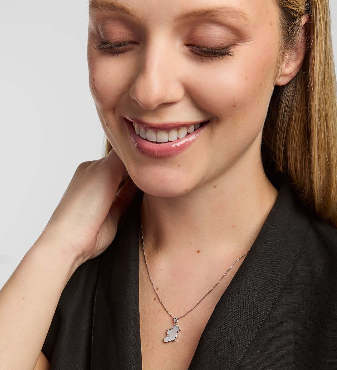 A female model wearing a Solvar map of Ireland necklace pendant, centred on the chest