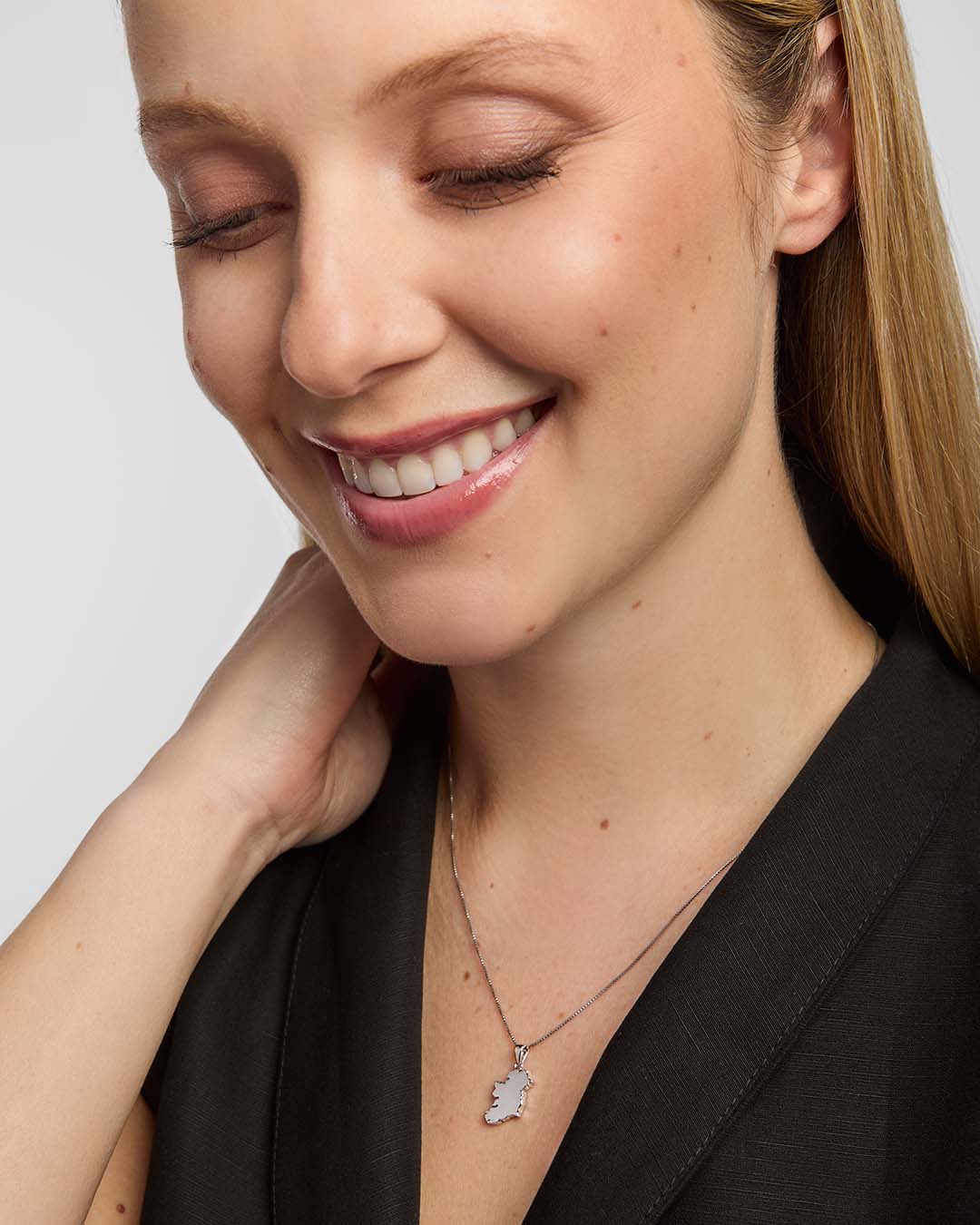 A close-up portrait of a female wearing a dark top and a fine chain necklace, featuring small map of Ireland pendant from Solvar, centred on the chest.