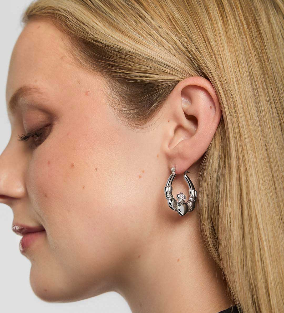 Close-up of a woman wearing a silver Claddagh hoop earring on a plain background