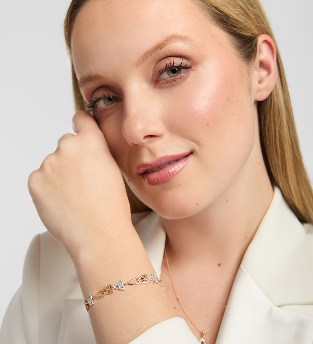 Close-up of a person wearing a white blazer, showing Solvar yellow gold bracelet with diamond-set Trinity knot links on the wrist, styled against neutral background.
