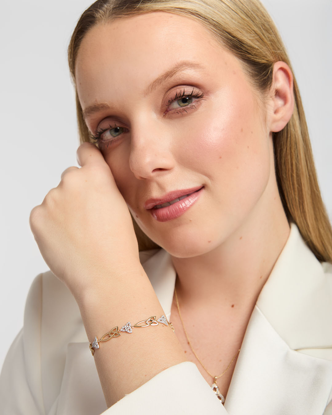 Close-up of a person wearing a white blazer, showing Solvar yellow gold bracelet with diamond-set Trinity knot links on the wrist, styled against neutral background.