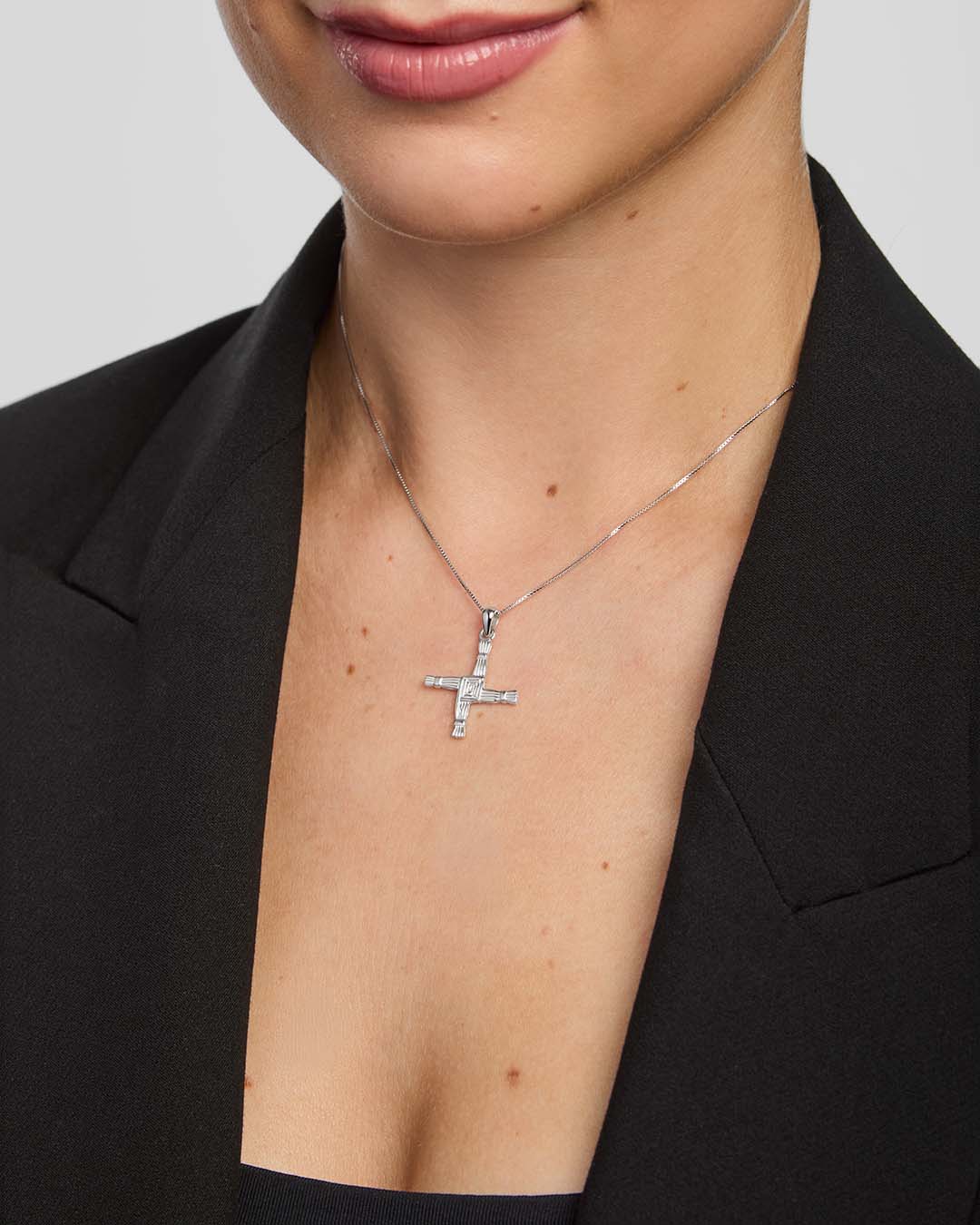 Person wearing a silver St Brigid's cross necklace against a neutral background