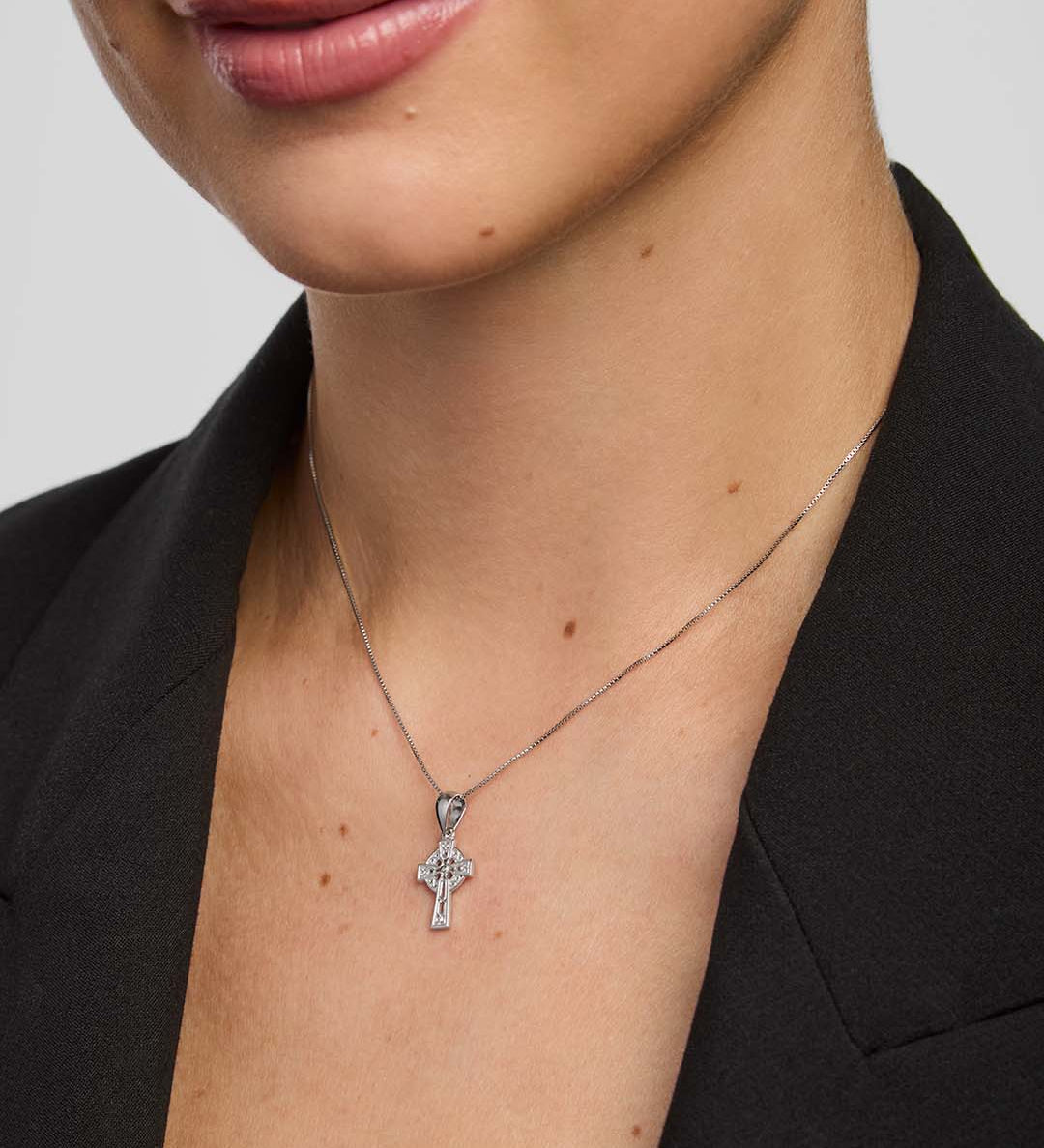 Close-up of a person wearing a small celtic cross necklace against a plain background