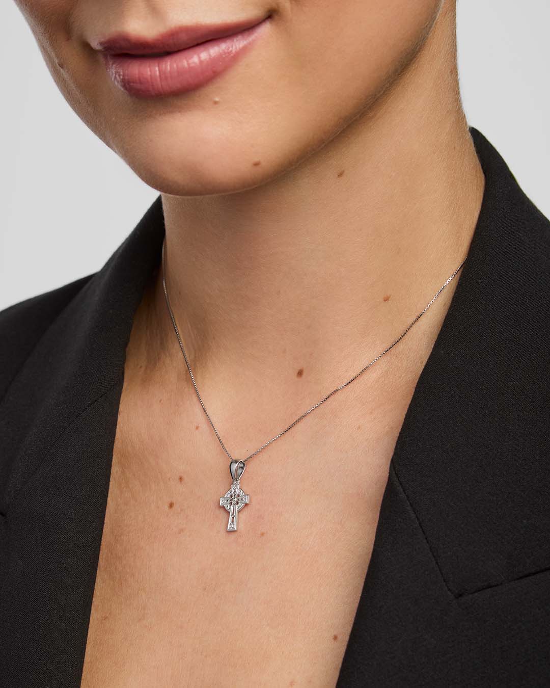 Close-up of a person wearing a small celtic cross necklace against a plain background