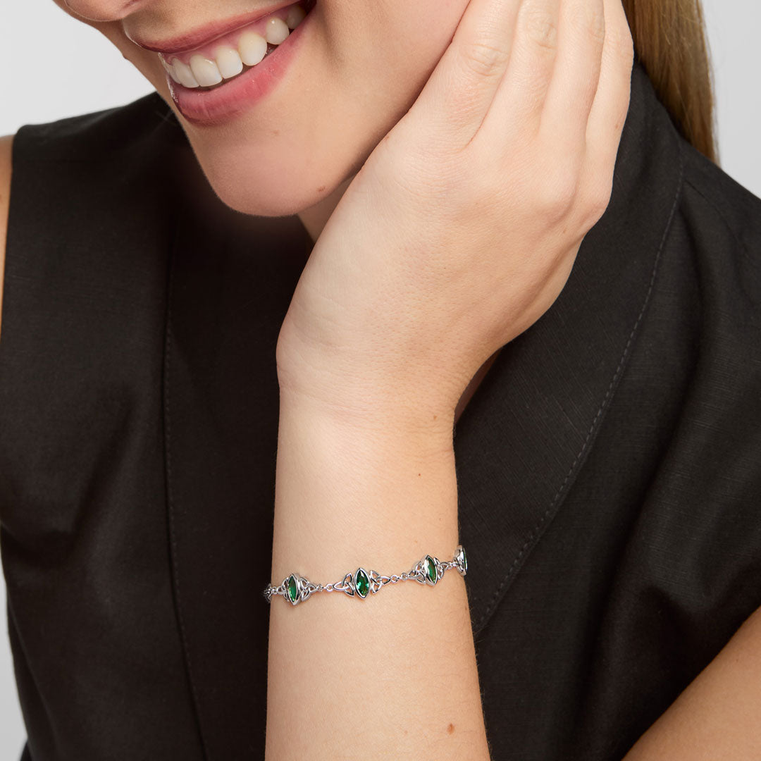 Close-up product photograph of a green cubic zirconia trinity knot bracelet on a woman’s wrist, emphasizing fine craftsmanship, luminous green stones, and an elegant Celtic design